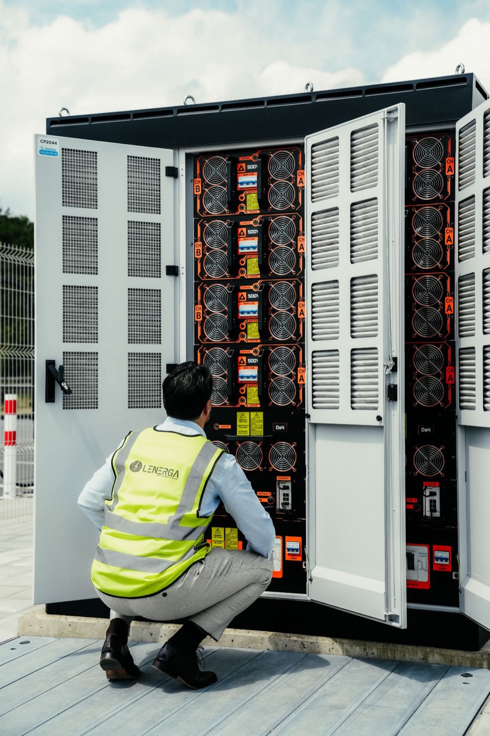 Lenerga technician in a high-visibility vest inspecting an open power cabinet for EV charging